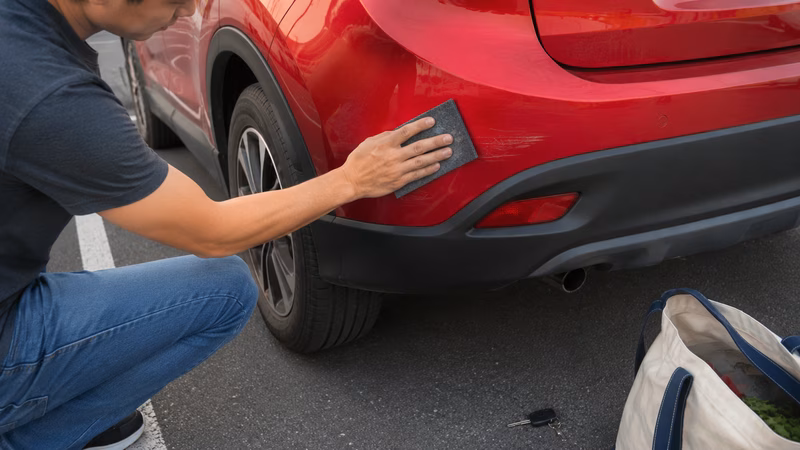 Eine Hand poliert mit einem Spezialtuch einen Kratzer im Autolack aus.